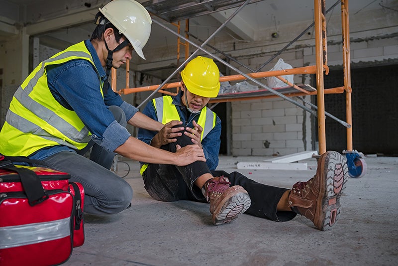 Construction worker helping an injured coworker at a job site.