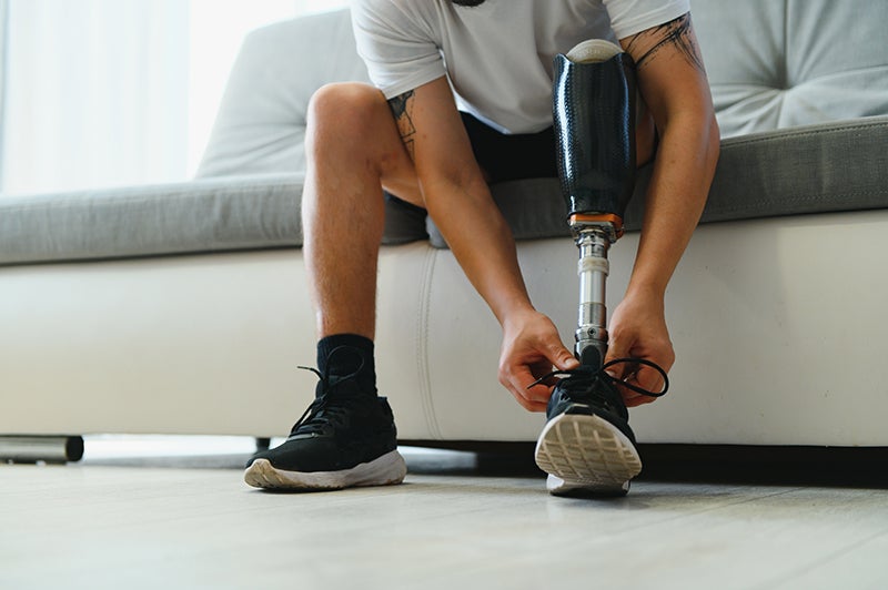 Man with prosthetic leg tying his shoe while sitting