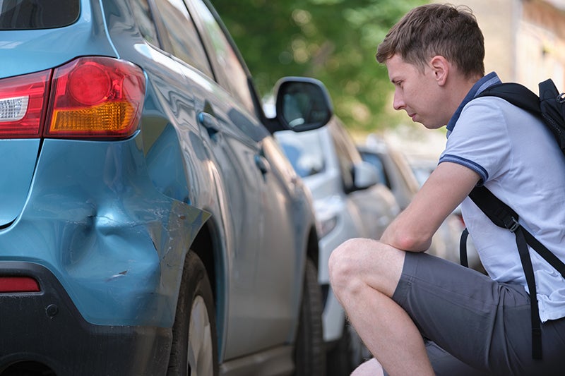 Man looks at damage on blue car bumper