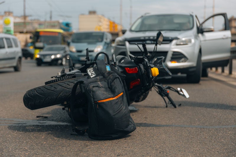 Motorcycle and backpack on road after accident with car.