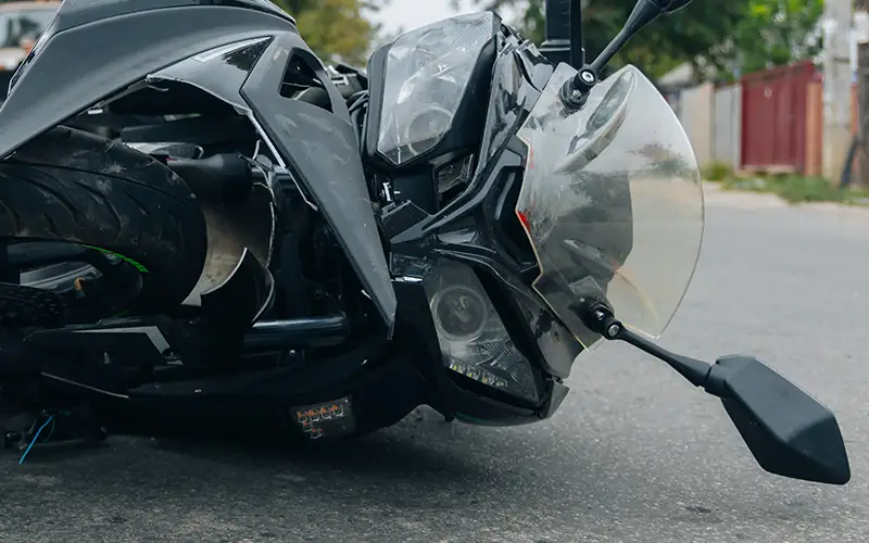 Black sport motorcycle with front damage lying on the asphalt.
