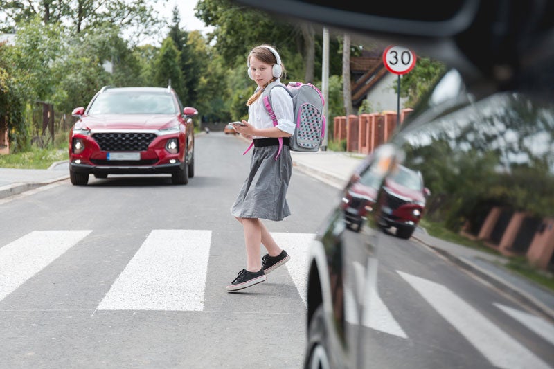 Young girl in headphones crossing road using a phone near car