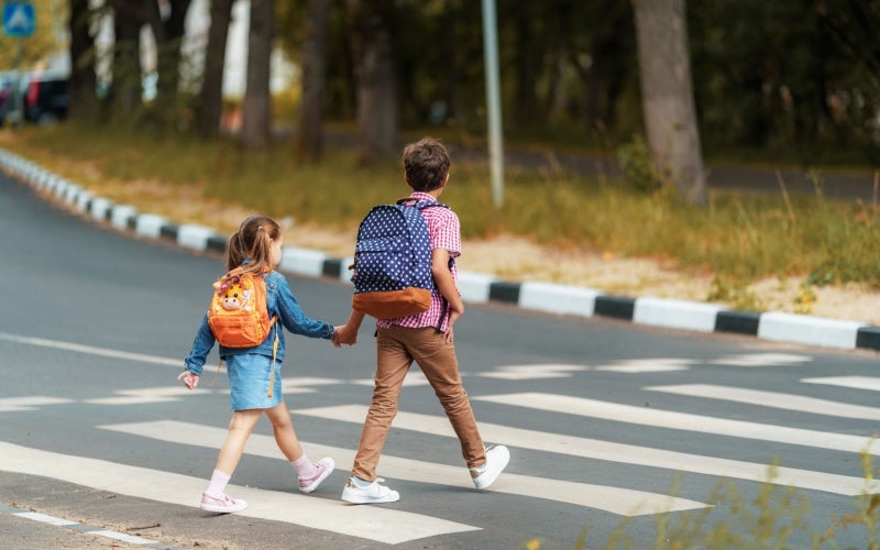 Boy and girl with backpacks holding hands crossing road.