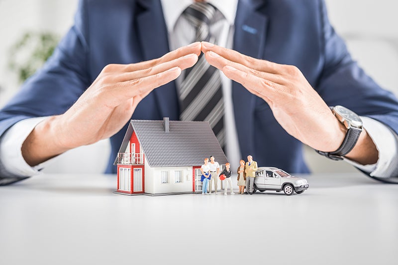 
Businessman's hands sheltering miniature house, family, and car.