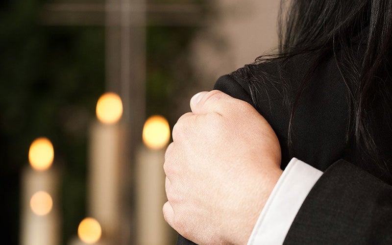 Hand on shoulder comforting person, with lit candles in background